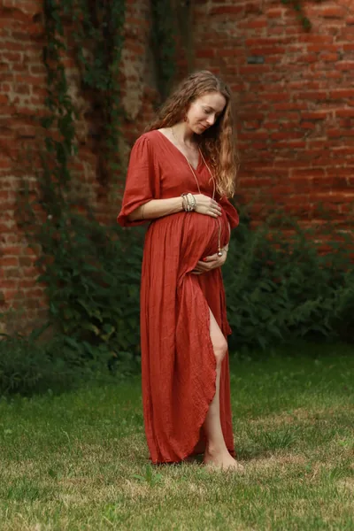 Těhotná Lucie v červených šatech u cihlové zdi
